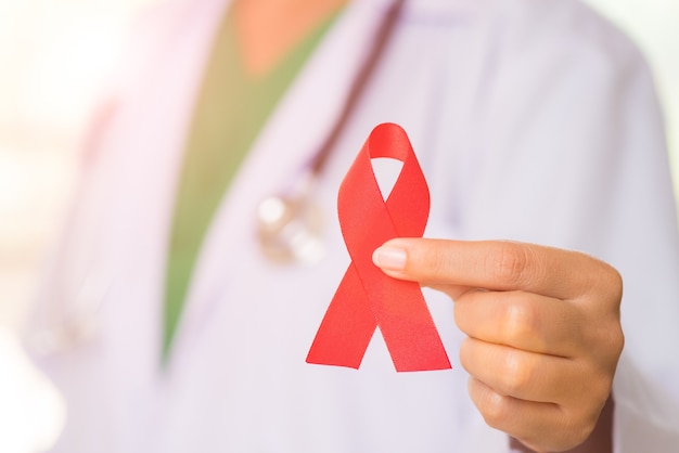 Female doctor with a stethoscope on shoulder holding red ribbon HIV