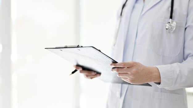 Female doctor with a stethoscope stands in the examination room holding a medical clipboard