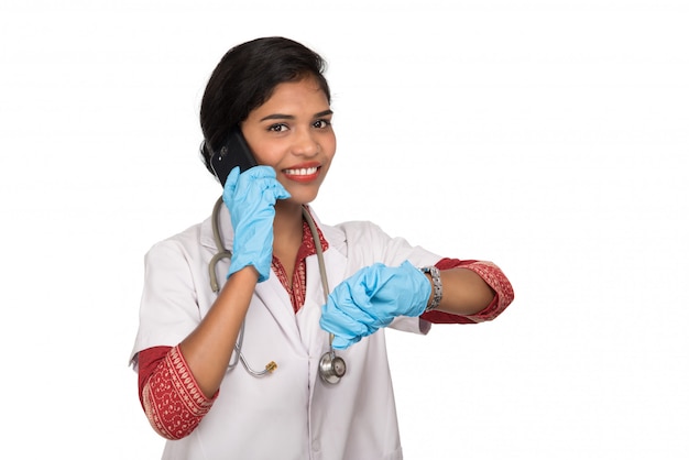 Female doctor with stethoscope talking on mobile phone on white wall