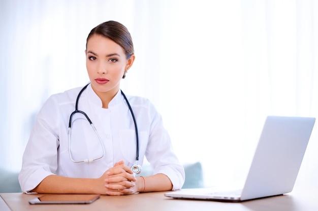 Female doctor with stethoscope wearing laboratory coat works in\
hospital and using laptop