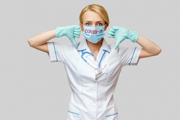 Female doctor with stethoscope wearing protective mask and latex gloves over light grey wall
