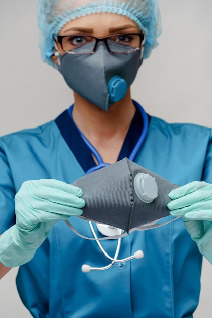 Female doctor with stethoscope wearing protective mask and latex gloves over light grey wall