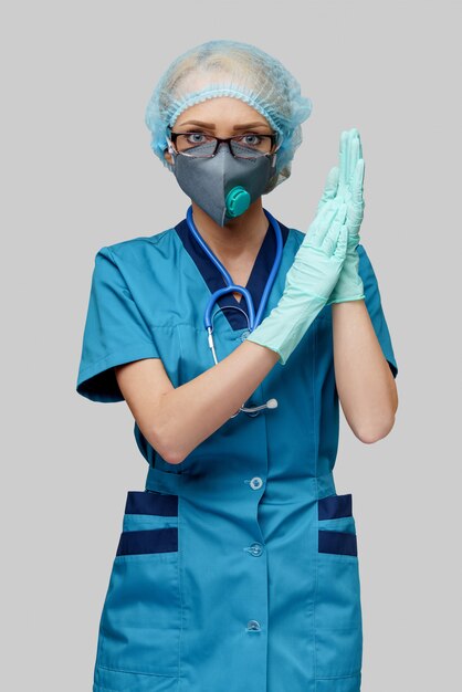 Female doctor with stethoscope wearing protective mask and latex gloves over light grey wall