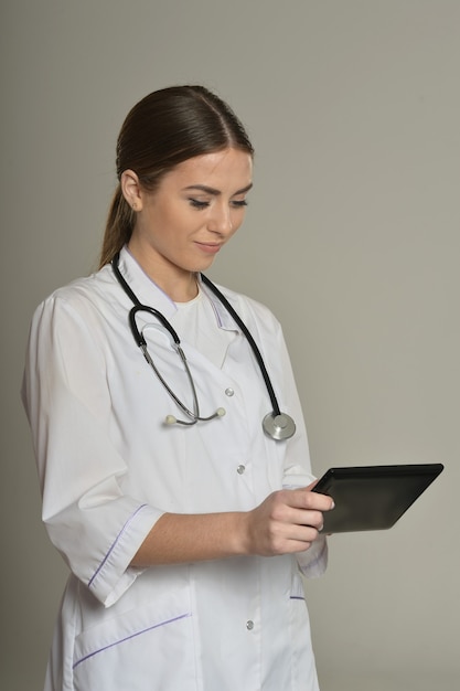 Female doctor with tablet pc, standing on grey background