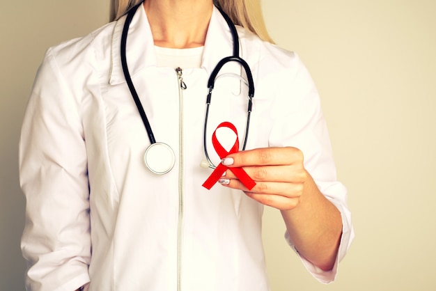 Female doctor withAID, HIV red ribbon. Cancer concept. Doctor Holds Red Ribbon to awareness world aids day Dec. 1. 