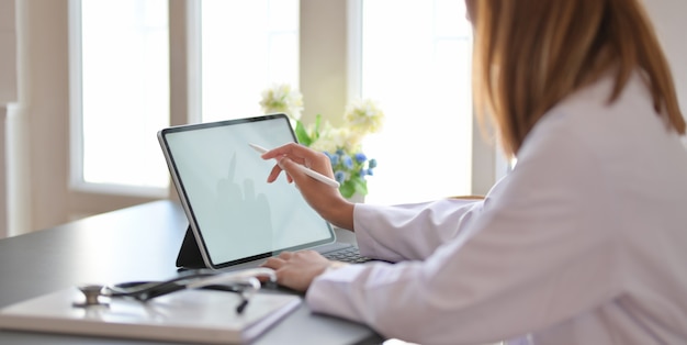 female doctor working with tablet and writing on paperwork in office room