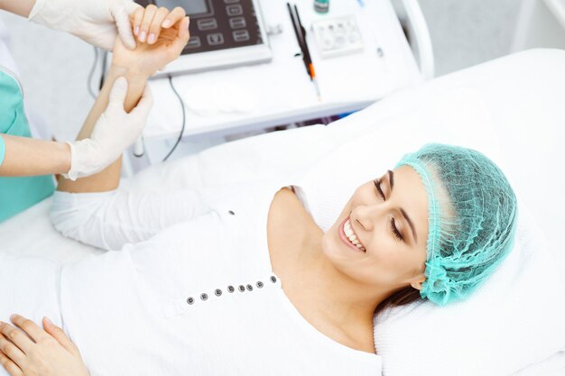 Female doctor and young woman patient in hospital. physicians\
examine girl pulse lying at the bed, view from above. medical help\
and insurance in health care, best treatment and medicine\
concept.