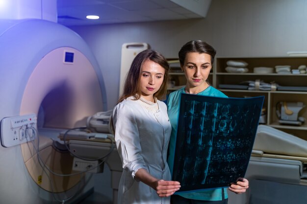 Photo female doctors discussing x-ray in modern medical room with computer tomography.