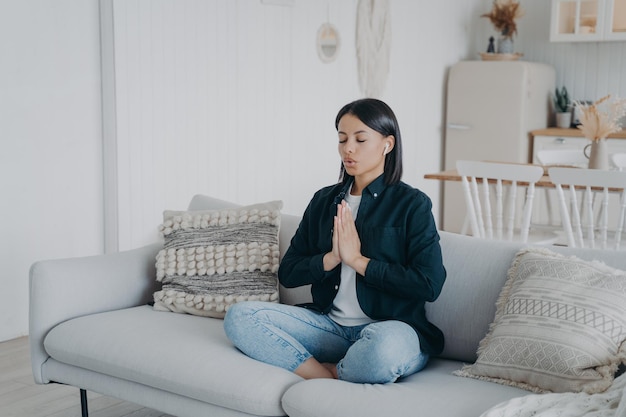 Female does breathing exercises meditating sitting in lotus pose on couch at home Stress relief