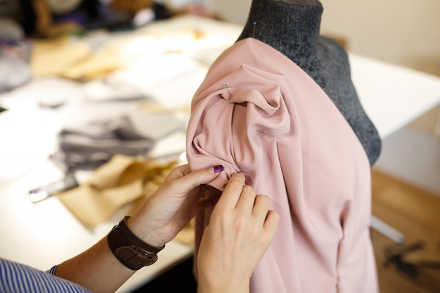 女性のドレスメーカーは、針で生地をマネキンに取り付けます。ドレスデザインの作成