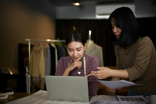 A female dressmaker using her laptop and working with her assistant in her workshop studio