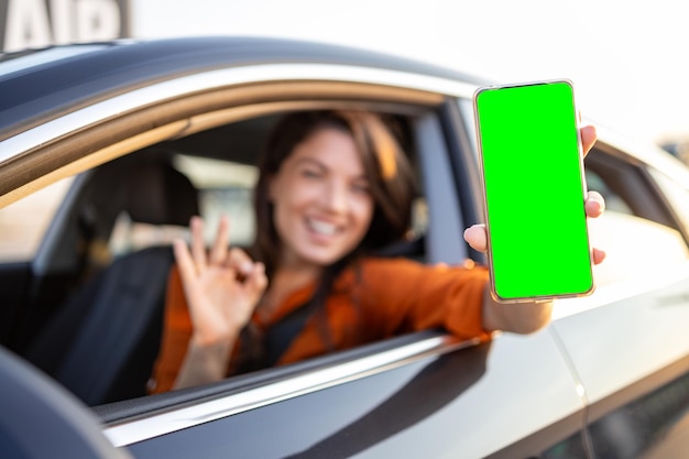 Photo female driver using digital app in mobile phone leaning out of the car window chroma key on device screen