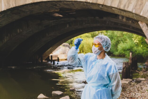 Foto l'ecologa o l'epidemiologo femminile esegue l'analisi dell'acqua in provetta in un fiume della città sotto il vecchio ponte