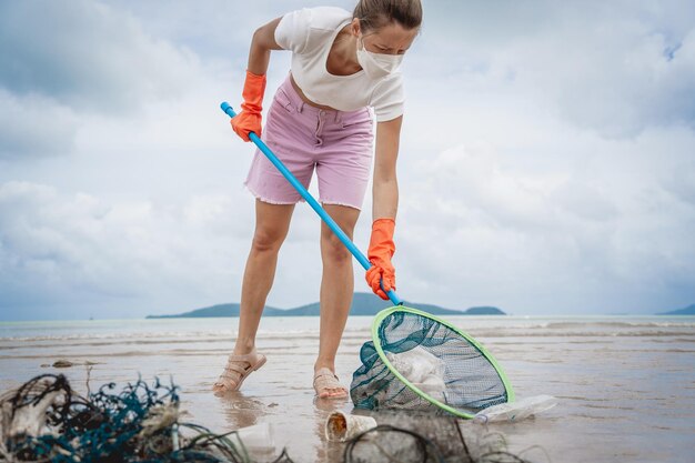 A female ecologist volunteer cleans the beach on the seashore from plastic and other waste