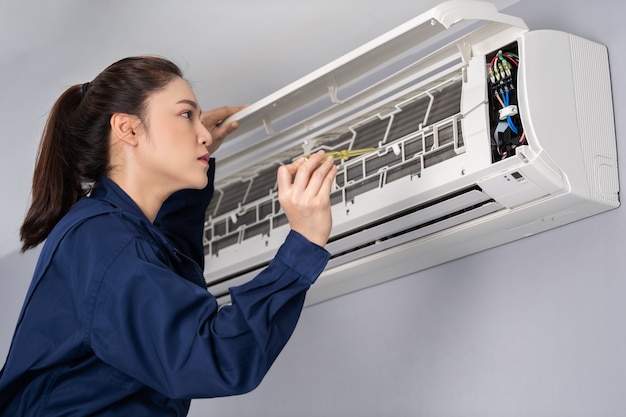 Female electrician with screwdriver repairing the air conditioner indoors