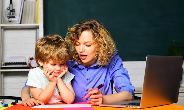 Female elementary school teacher helping little boy with writing lesson in classroom at school