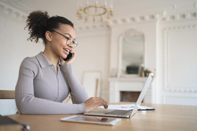 A female employee in the office with glasses works uses a\
laptop answers the client\'s mail and phone