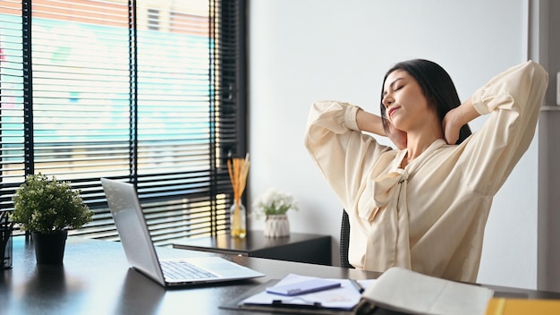 Female employee relaxing at work reclining back in chair and stretching her arms