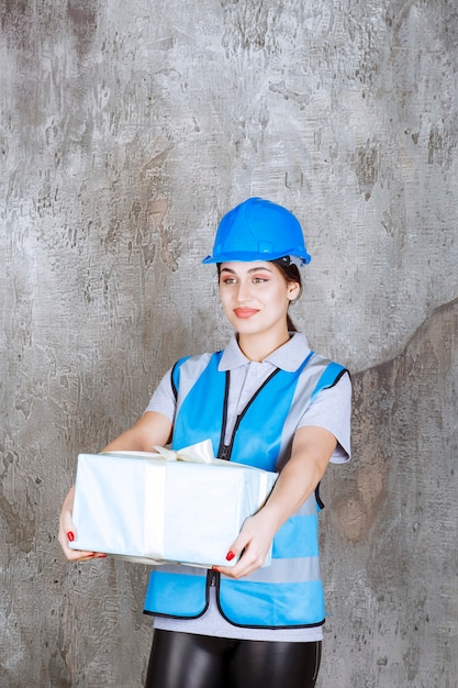 Female engineer in blue uniform and helmet holding a blue gift box.