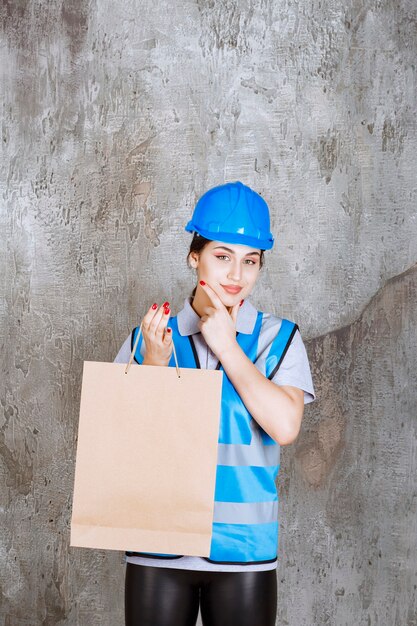 Female engineer in blue uniform and helmet holding a shopping bag and looks thoughtful.