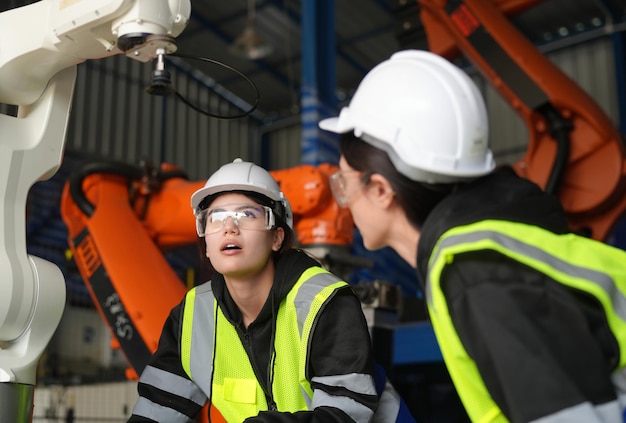 L'ingegnere femminile controlla e controlla la macchina dei bracci robotici di automazione in una fabbrica industriale intelligente sulla robotica del software di sistema di monitoraggio in tempo reale e sulle operazioni di produzione digitale