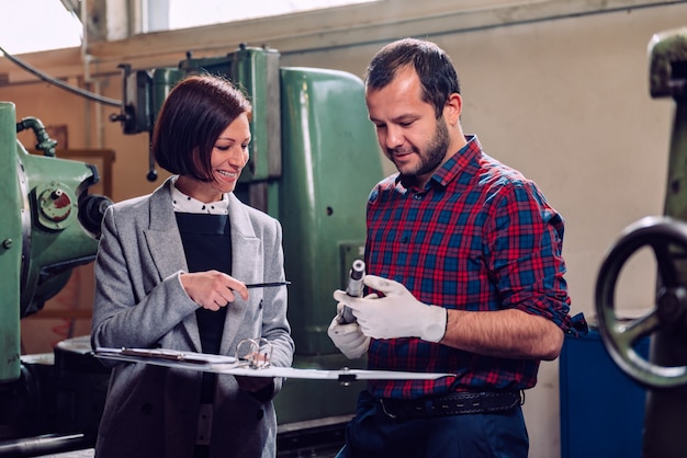 Female engineer consulting with machinist holding gear shaft