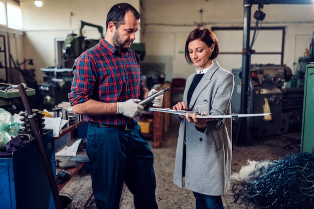 Female engineer consulting with machinist holding manufactured part