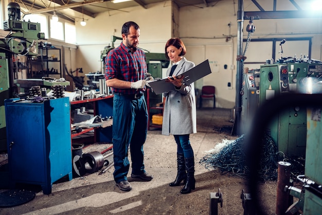 Female engineer consulting with machinist measuring gear shaft diameter