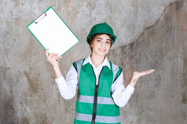 Ingegnere femminile in uniforme verde e casco che dimostra l'elenco dei progetti.