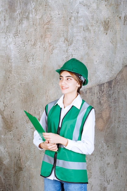 Female engineer in green uniform and helmet holding a green project folder.