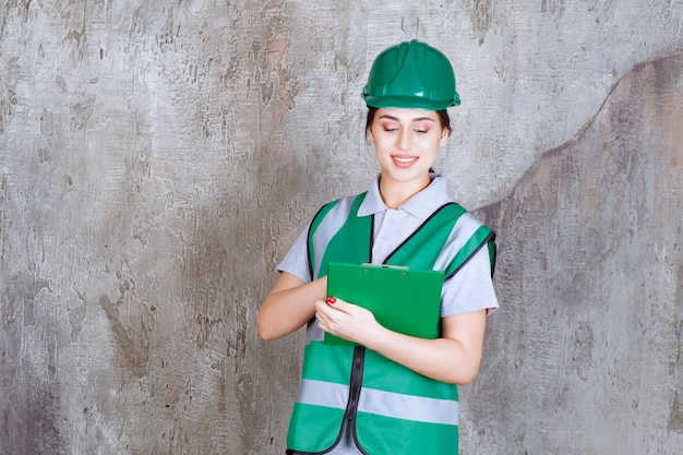 Ingegnere femminile in uniforme verde e casco che tiene la cartella del progetto.