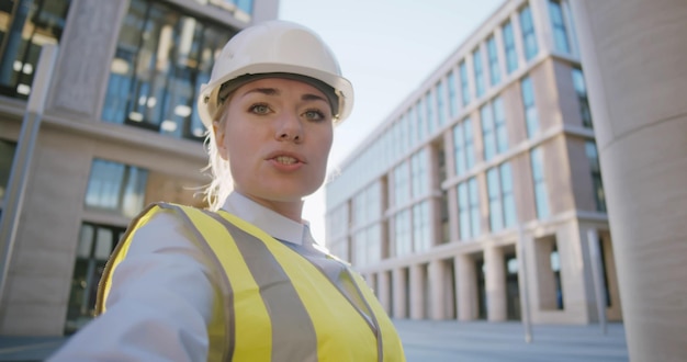 female engineer in hardhat making video call to client standing outdoors at construction site