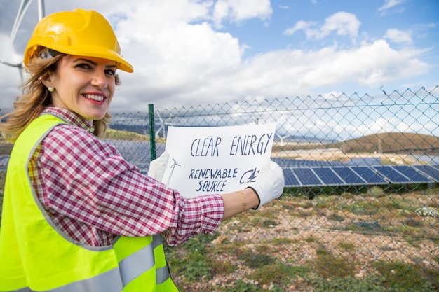 太陽光発電所でクリーン エネルギーの再生可能エネルギー源と書かれたシートを持っている女性エンジニア