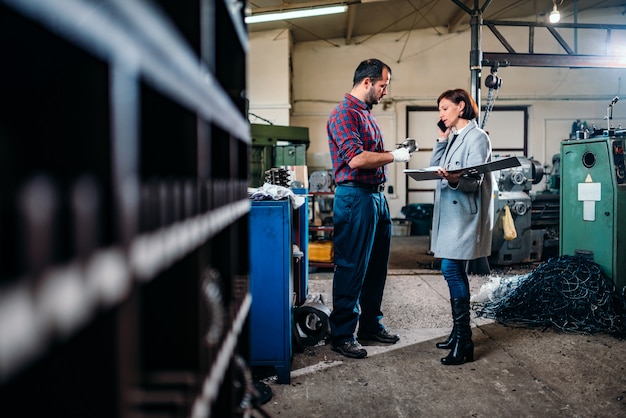 Female engineer standing with machinist and talking on the phone with client