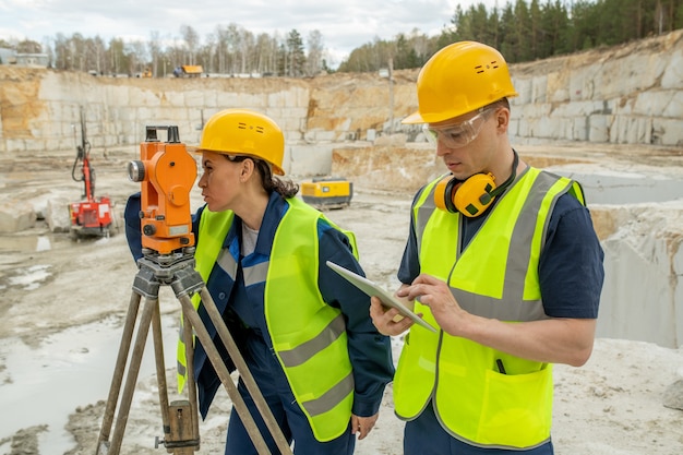 Photo female engineer using geodetic station while her colleague scrolling in tablet