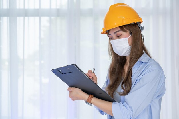 Female Engineer wear face mask with safety yellow helmet check the correctness of the construction