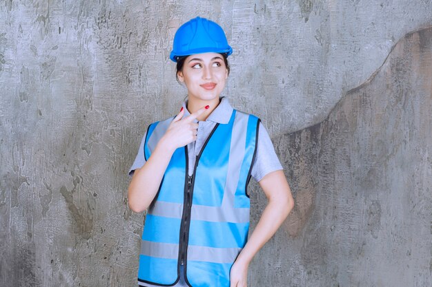 Female engineer wearing blue helmet and gear and showing something on the right.