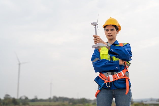 Mulino a vento ingegnere femminile in uniforme e sicurezza del casco che tiene modello di turbina eolica