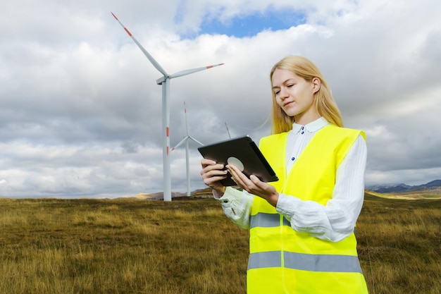 태블릿을 들고 있는 여성 엔지니어가 풍력 터빈의 작동을 조정합니다. 청정 에너지