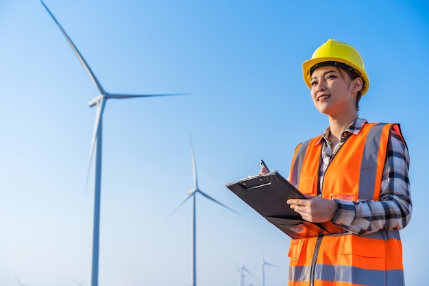 Female engineer working and writing on a clipboard against wind turbine farm