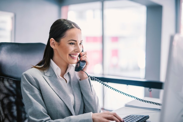 A female entrepreneur typing on keyboard having phone call and multitasking at office