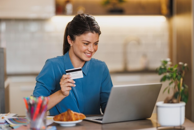 Photo female entrepreneur working on laptop and paying bills with credit card while working from her home office.