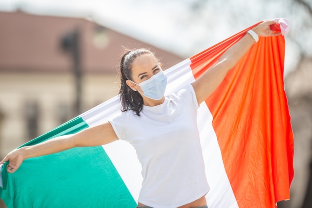 La donna con la maschera facciale tiene la bandiera italiana su una strada che celebra la revoca delle restrizioni attuate a causa di un coronavirus.