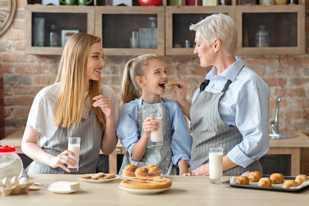 Female family spending time together on weekend at kitchen, mom, daughter and granny eating pastry