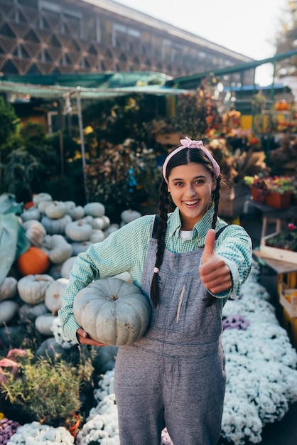 Female farmer holding pumpkin showing thumb up