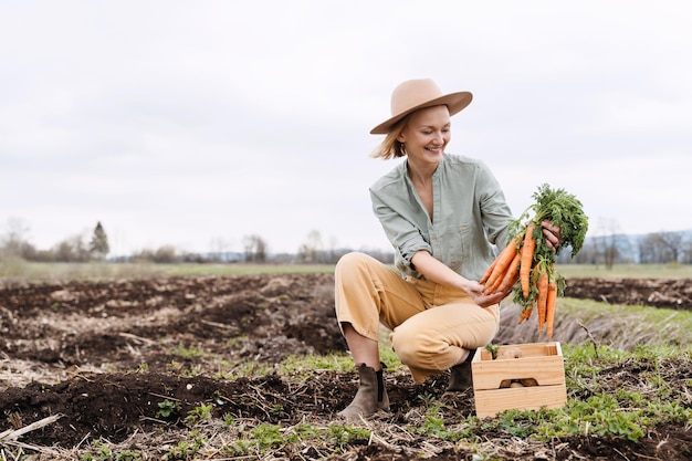 Photo female farmer holding wooden box full of fresh raw vegetables in agricultural field area