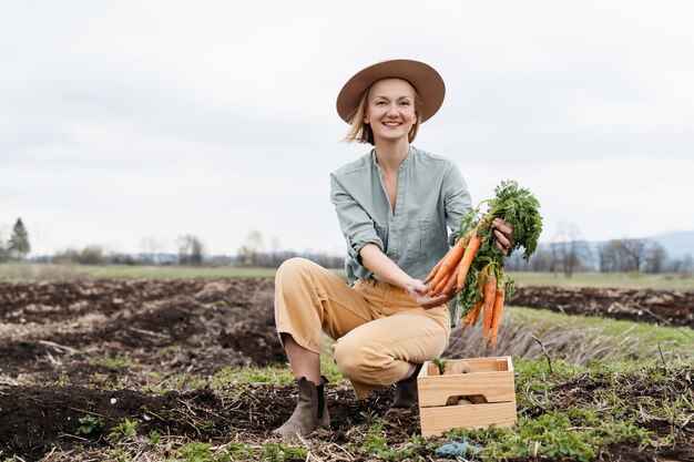 Photo female farmer holding wooden box full of fresh raw vegetables in agricultural field area