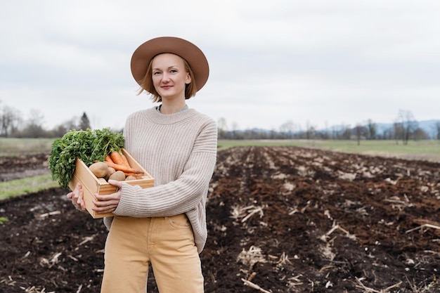 Photo female farmer holding wooden box full of fresh raw vegetables in agricultural field area