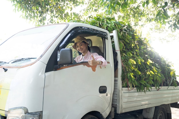 写真 親指を立てて帽子をかぶった女性農家が保育園の苗運搬車に乗る