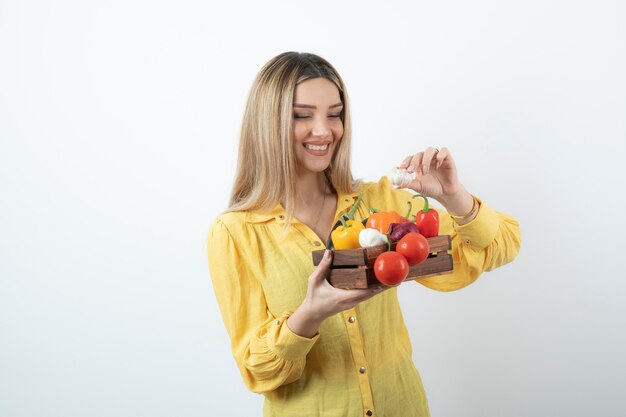 Female farmer standing and holding a wooden crate full of a variety of organic vegetables